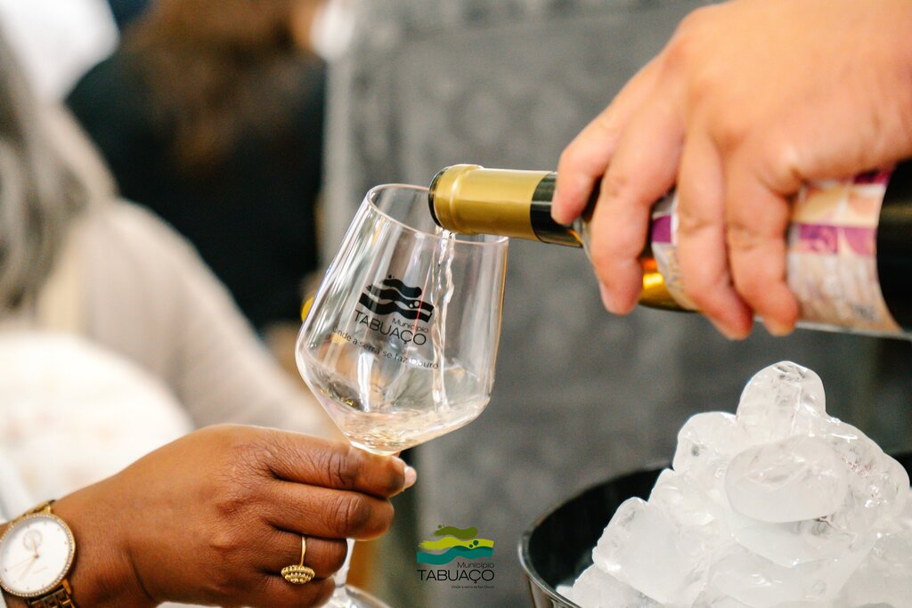 Pessoa a servir vinho branco num copo com logótipo “Município de Tabuaço”.