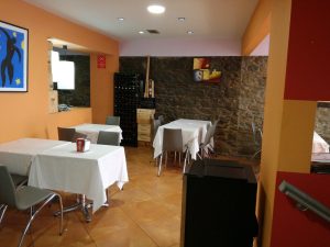 Interior do Restaurante Bilheteira com mesas cobertas por toalhas brancas, cadeiras cinzentas, paredes laranja com apontamentos em pedra e quadros decorativos.