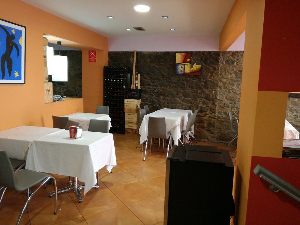 Interior do Restaurante Bilheteira com mesas cobertas por toalhas brancas, cadeiras cinzentas, paredes laranja com apontamentos em pedra e quadros decorativos.