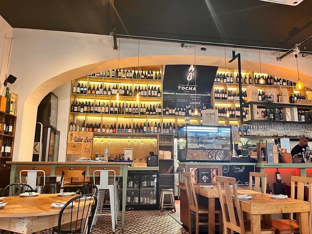 Espaço que traduz o conceito de tasca moderna e wine bar da Casa da Tocha, reunindo garrafeira iluminada, mesas preparadas e ambiente acolhedor que reforça a harmonização entre petiscos, vinhos e tradição algarvia.