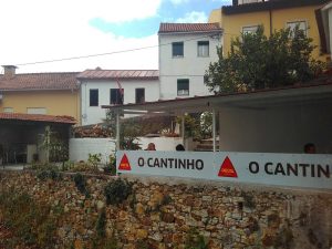 Fachada do Restaurante O Cantinho com esplanada coberta, clientes sentados e edifícios residenciais ao fundo.