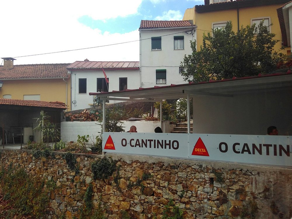 Fachada do Restaurante O Cantinho com esplanada coberta, clientes sentados e edifícios residenciais ao fundo.