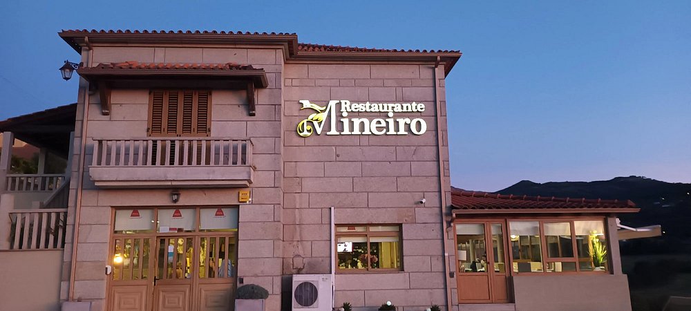 Fachada de dois pisos em pedra, com portas e janelas em madeira, telhado vermelho e letreiro iluminado do restaurante.