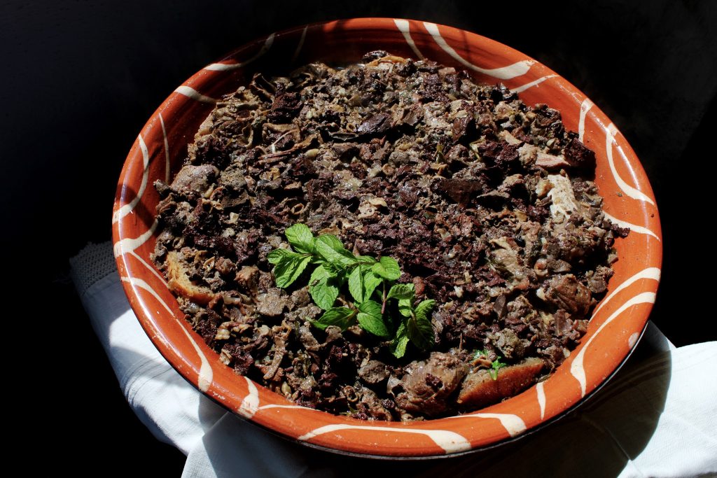 Taça de barro com prato de carne em molho escuro, decorado com ervas frescas.