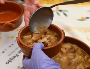 Concha de metal a servir migas de feijão suculentas numa tigela de barro individual.