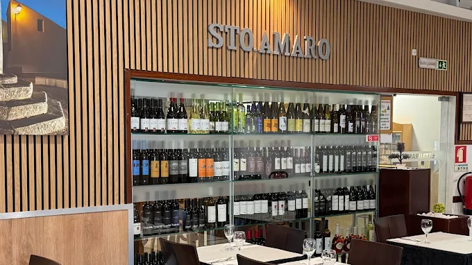 Salão interno do restaurante Sto. Amaro com parede decorada em painéis de madeira vertical, grande vitrine de garrafeira com vinhos e mesas postas.
