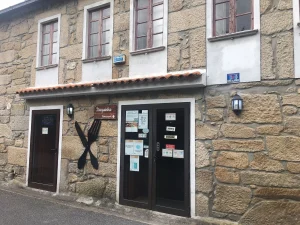 Fachada de pedra com portas de madeira, letreiro “Tasquinha Restaurante”, talheres decorativos e placas, em rua do centro histórico.