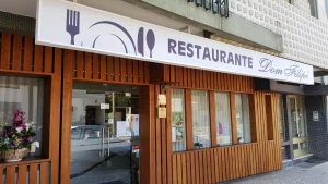 Fachada do Restaurante Dom Filipe com portas de vidro, revestimento em madeira e letreiro com utensílios de mesa e nome do estabelecimento.