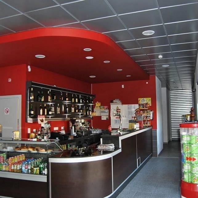 Balcão de café e bar com vitrine de bebidas e salgados, prateleiras com garrafas e paredes vermelhas em ambiente interno moderno.