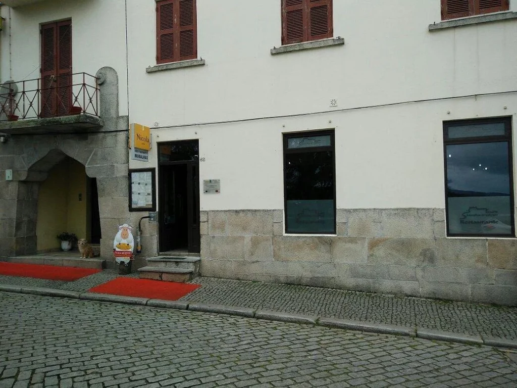 Fachada de restaurante em prédio de dois andares, com portas e janelas de madeira, entrada sinalizada e rua de paralelepípedos.
