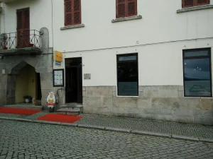 Fachada de restaurante em prédio de dois andares, com portas e janelas de madeira, entrada sinalizada e rua de paralelepípedos.