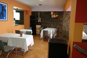 Interior do Restaurante Bilheteira com mesas cobertas por toalhas brancas, cadeiras cinzentas, paredes laranja com apontamentos em pedra e quadros decorativos.