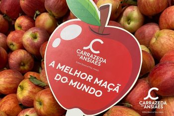 Pilha de ma&ccedil;&atilde;s vermelhas com placa vermelha em forma de ma&ccedil;&atilde; com texto promocional.