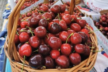 Cesto de vime cheio de cerejas vermelhas e escuras com caules verdes.