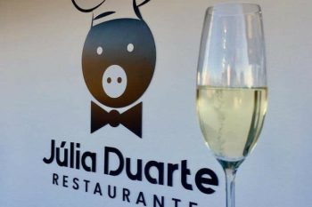 Logótipo do Restaurante Júlia Duarte numa parede, com copo de vinho branco em primeiro plano.