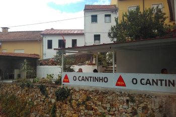 Fachada do Restaurante O Cantinho com esplanada coberta, clientes sentados e edifícios residenciais ao fundo.