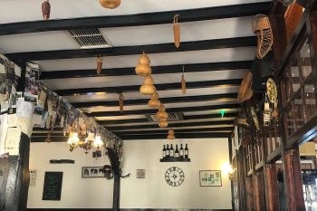 Sala de restaurante com mesas postas, teto com vigas escuras e decoração tradicional com abóboras secas e garrafas.