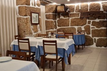 Sala com mesas cobertas por toalhas azuis e brancas, paredes de pedra e elementos decorativos rústicos.