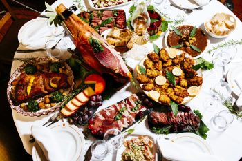 Mesa com presunto em suporte, enchidos, queijos, fritos, uvas e pão.